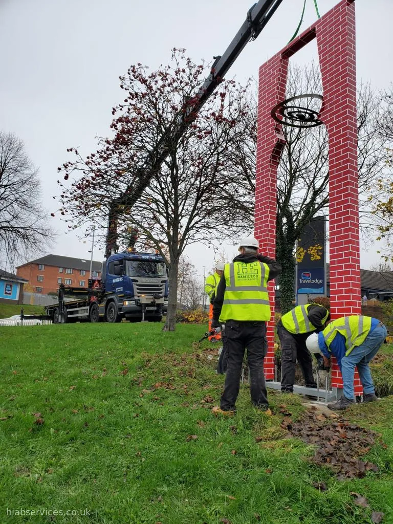 HIAB crane and crew installing a tall signage column on site, UK